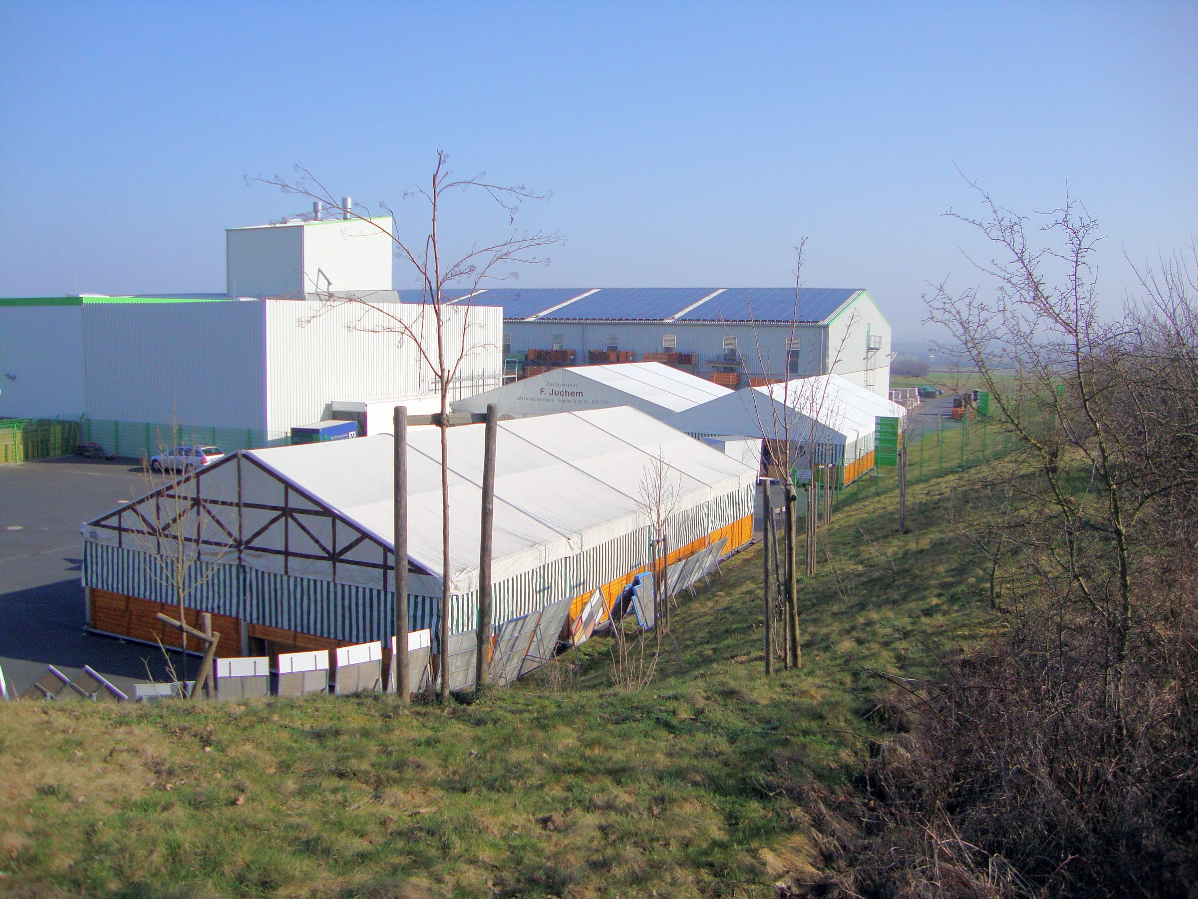 Several adjoining tents next to a company building, seen from an embankment
