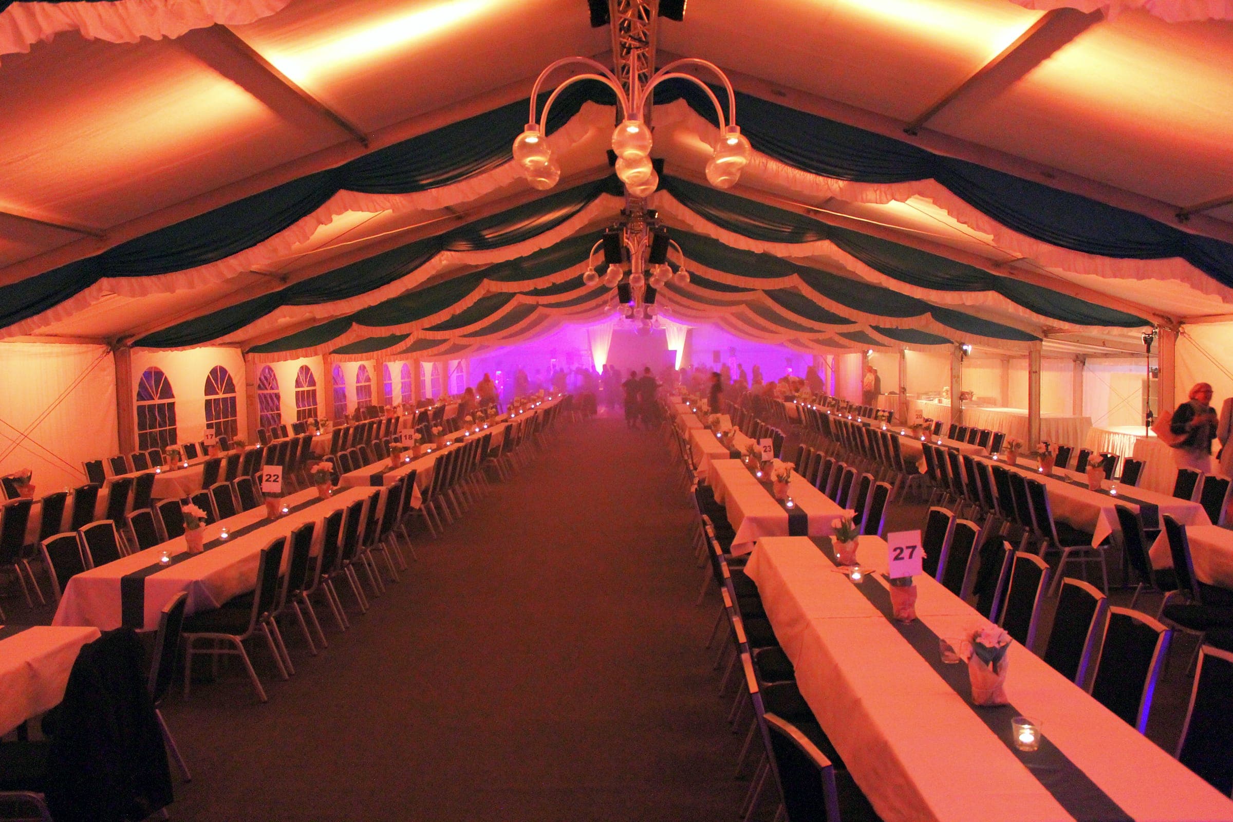 Marquee in the evening with long tables, green-and-white ceiling decoration and warm lighting