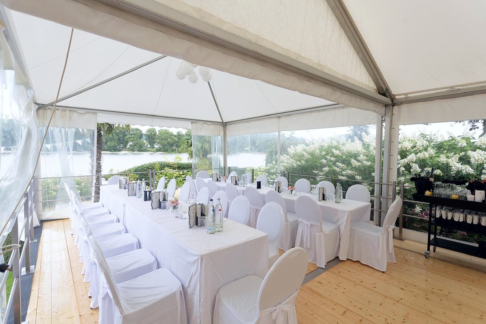 Festively laid table with white chair covers in a tent, a view of the water through the side wall