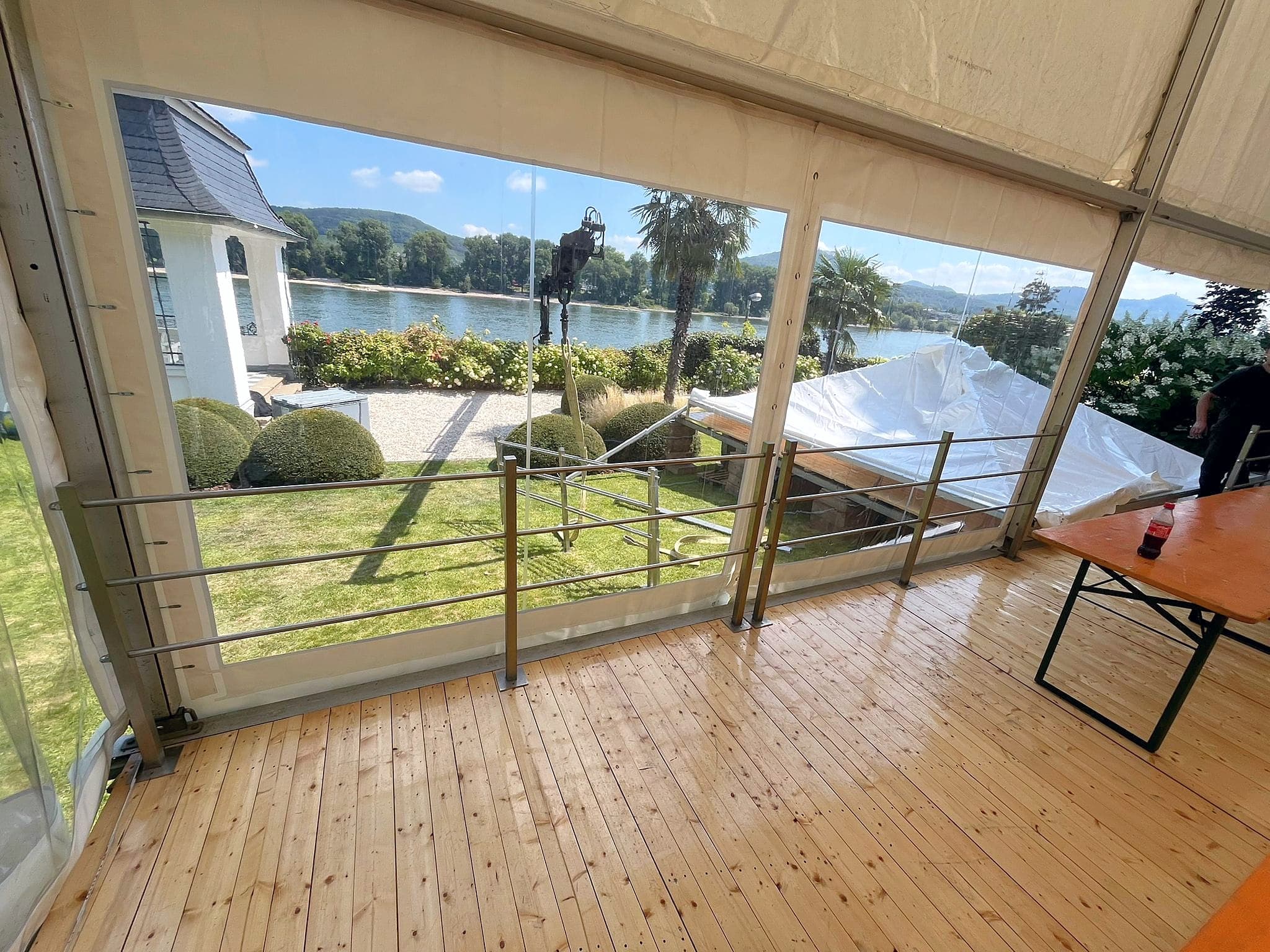 Blick aus einem Pavillon mit Holzboden und Geländer über einen Garten auf den Rhein