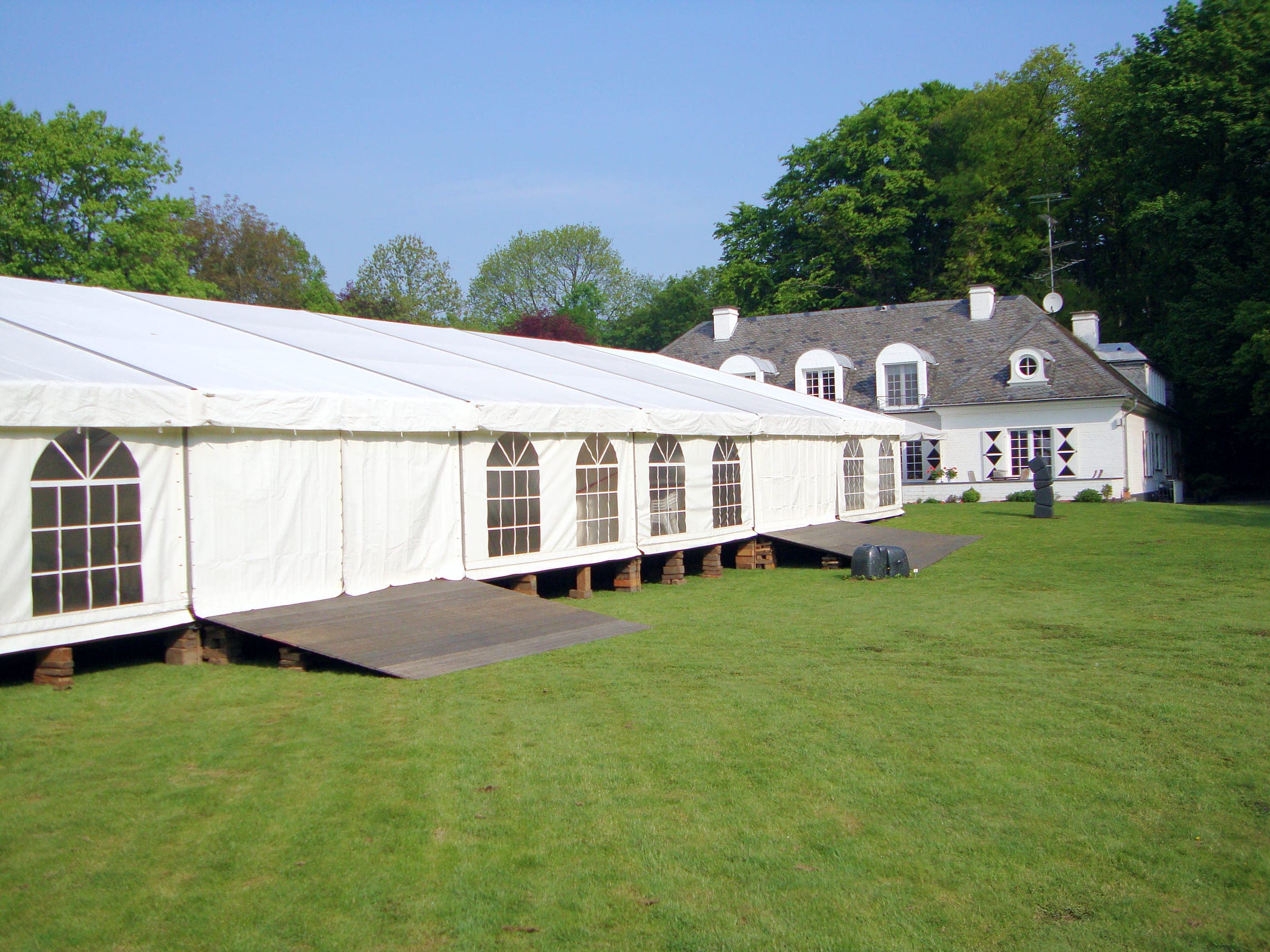 Langes weißes Zelt mit Sprossenfenstern auf einem Unterbau im Park vor einem Herrenhaus