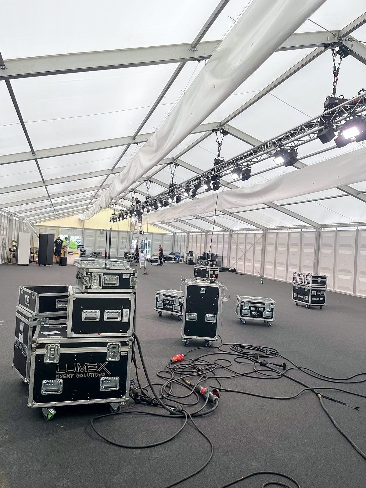 Große Zelthalle im Aufbau: Traversen mit Scheinwerfern unter dem Dach, Flightcases und Kabel auf dem dunklen Boden