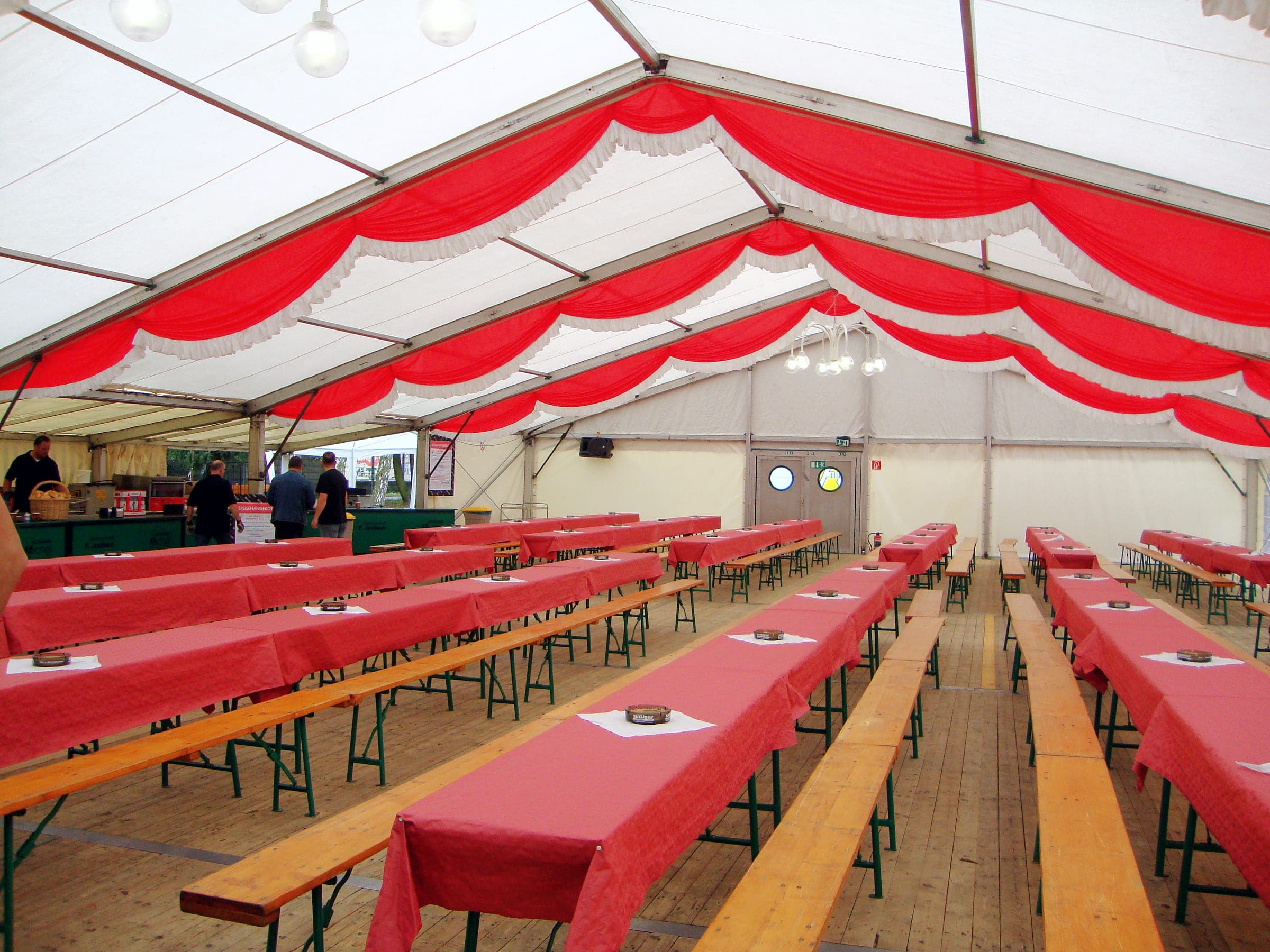 Festzelt mit rot-weißer Deckendeko, Festzeltgarnituren mit roten Tischdecken und Holzboden