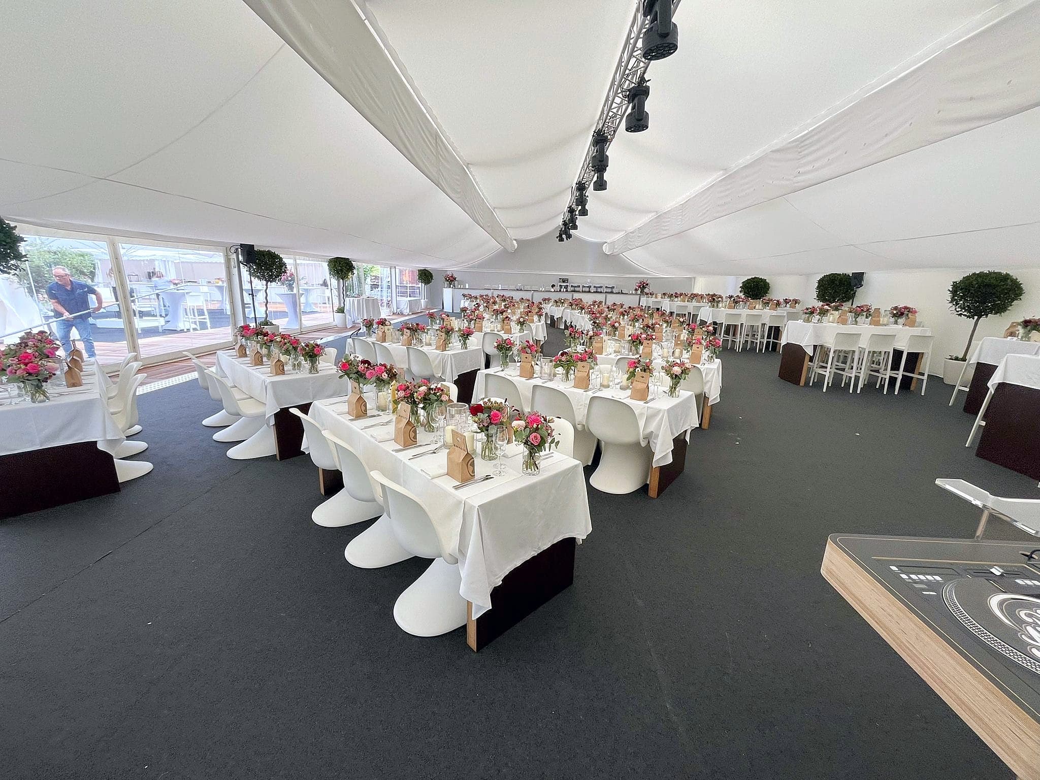 Gala-Tafeln mit weißen Decken und Blumen, dunkler Teppichboden, Lichttechnik unter dem Zeltdach