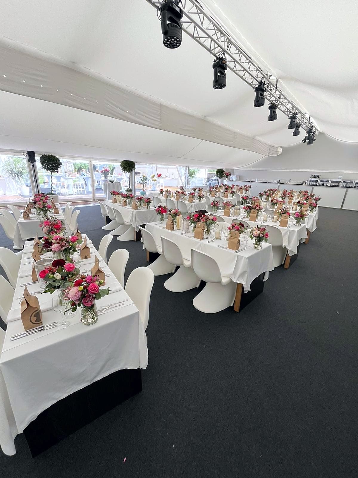 Festlich eingedecktes Zelt mit langen Tafeln, Blumengestecken und weißen Schalenstühlen auf dunklem Teppich, unter dem Dach eine Traverse mit Scheinwerfern