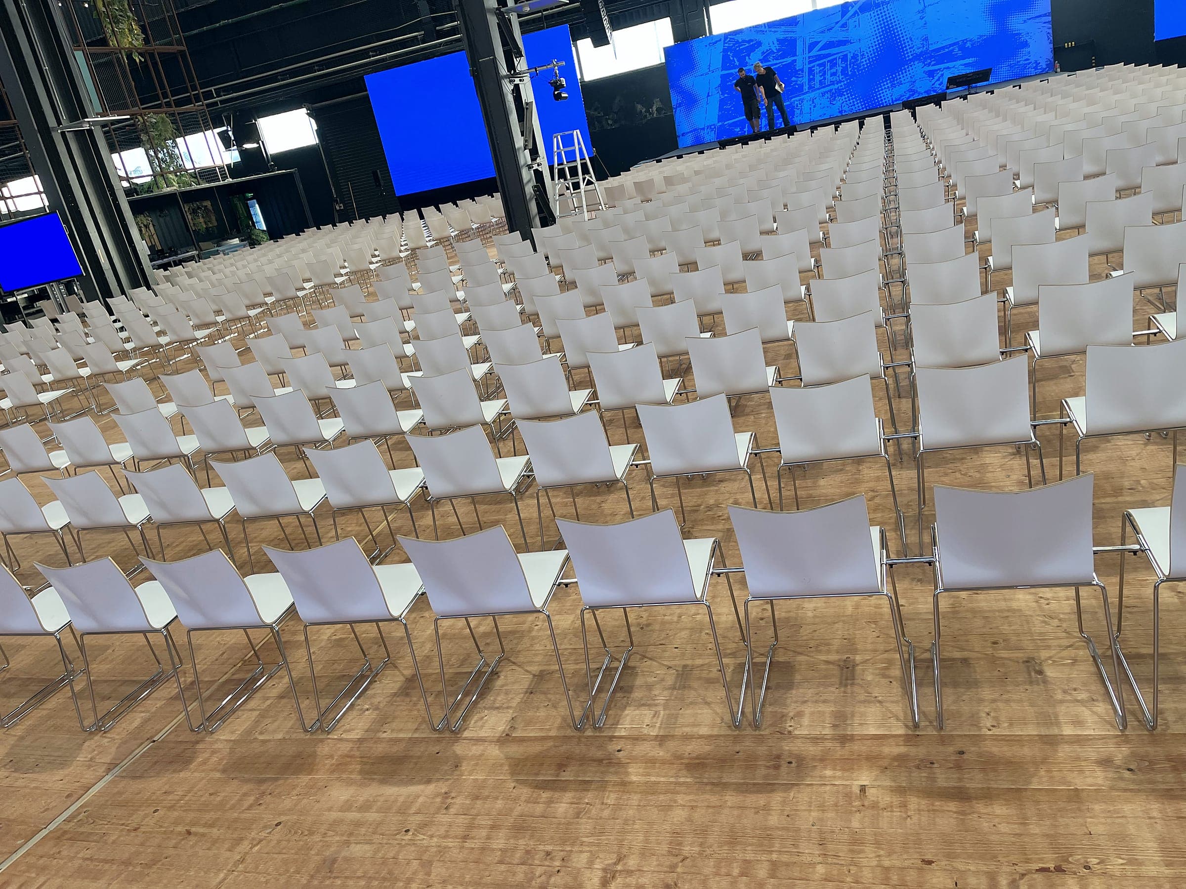 Reihenbestuhlung mit weißen Stühlen auf Holzboden vor einer Bühne mit LED-Wänden